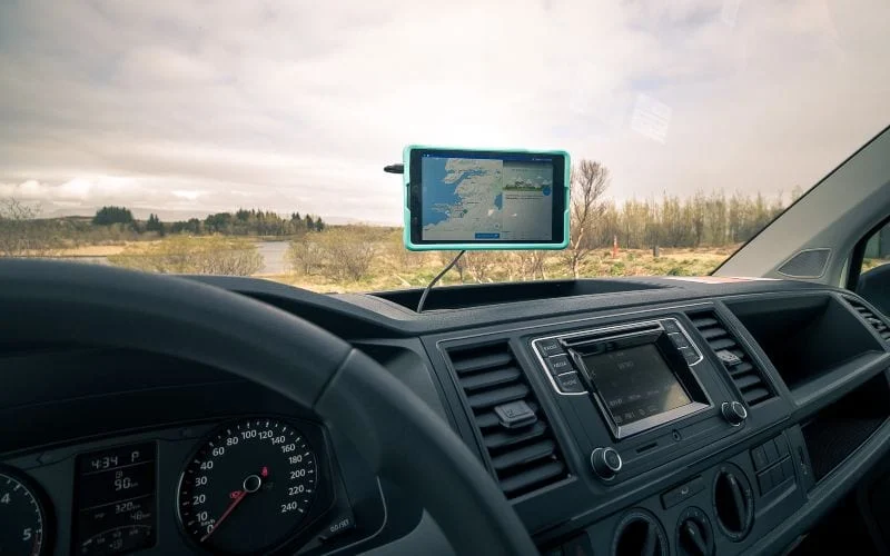 A tablet showing a navigation map mounted on a van dashboard, with a lake and grassy field visible outside