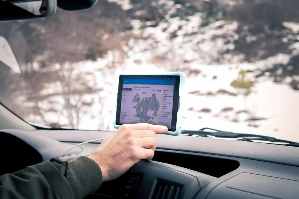 A hand holding a rugged tablet mounted on a car dashboard, showing a weather forecast map, with snow outside